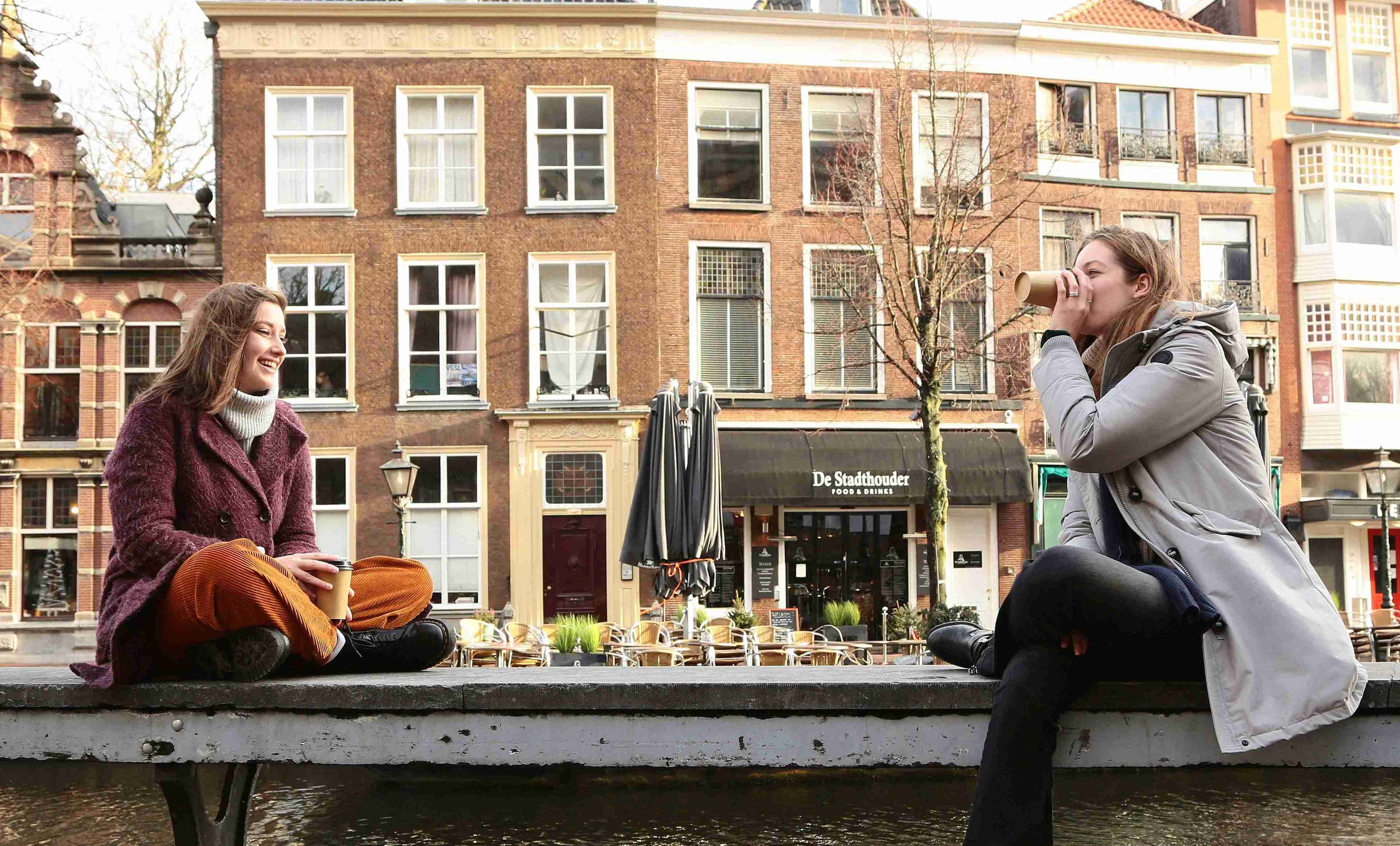 Two women sat outside on the canals drinking a coffee