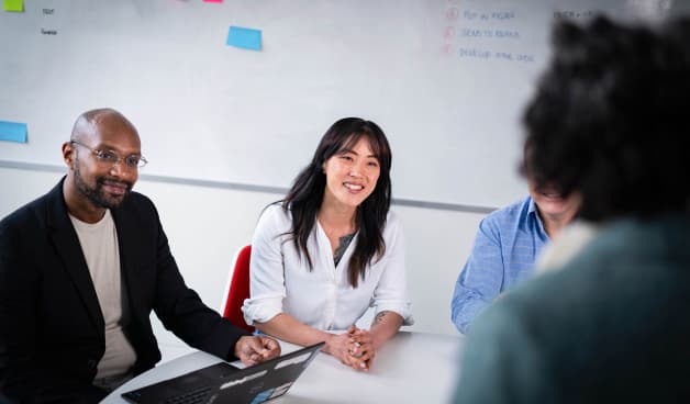 Group in a meeting room at a workplace sitting round a table smiling and learning