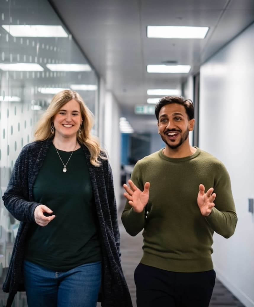 Two colleagues walking through an office corridor, smiling and talking together.